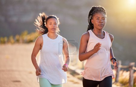 Foto de Dos jóvenes atletas enfocadas hacia fuera para una carrera en un camino de montaña en un día soleado. Mujeres jóvenes enérgicas corriendo al aire libre para ayudar a sus cuerpos en forma y en forma. Dos deportistas haciendo ejercicio juntas. - Imagen libre de derechos