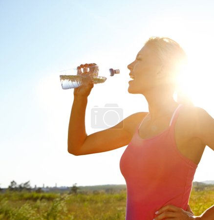 Foto de Mantenerse hidratada durante su entrenamiento. Una hermosa joven en ropa deportiva bebiendo agua de una botella - Imagen libre de derechos