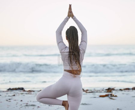 Téléchargez les photos : Yoga, fitness et entraînement à la plage avec une femme noire en pose d'arbre pour l'exercice, l'équilibre et la méditation zen pour la santé et le bien-être en plein air dans la nature. Dos de la femme pour l'entraînement de chakra pour un corps sain. - en image libre de droit