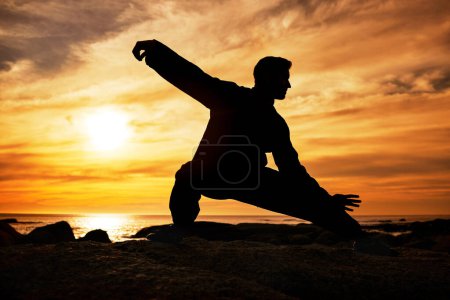 Foto de Hombre de karate, silueta y tai chi con cielo al atardecer en el horizonte de la playa para las artes marciales, taekwondo o ejercicio de lucha, entrenamiento o práctica. Art deco de atleta en el mar para el entrenamiento de la naturaleza y la aptitud. - Imagen libre de derechos