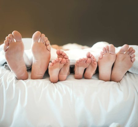 Photo for Comfy family lying in a bed together relaxing taking a nap together. Feet and toes of parents and their children being lazy and resting on a bed together during the day at home. - Royalty Free Image