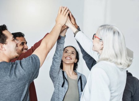 Photo for Diverse group of five businesspeople smiling giving each other a high five in a meeting in an office at work. Happy women and men joining their hands in unity standing together while working. - Royalty Free Image