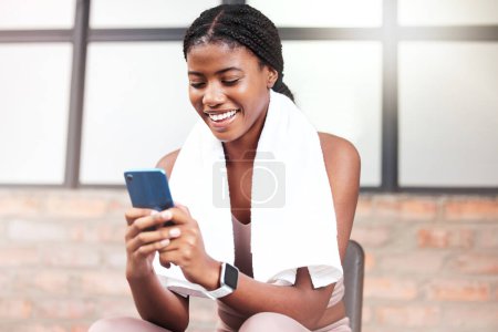 Photo for Fitness, phone and black woman relax in gym tracking workout, progress or exercise on app. Sports, mobile tech and happy female with towel and smartphone internet browsing, social media or texting - Royalty Free Image