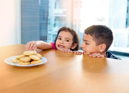 Photo for Shes got naughty little fingers. two mischievous young children stealing cookies on the kitchen table at home - Royalty Free Image