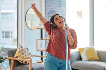 Music, headphones and woman singing while cleaning home, dancing and having fun. Singer, dance and female spring cleaning for hygiene holding broom like microphone, sweeping dust and streaming radio