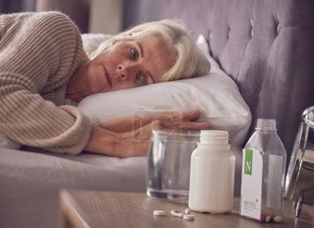 Elderly woman, bed and medical addiction with pills, medicine or medication while lying awake at home. Senior female suffering from sick, illness or mental health, trauma or disorder in the bedroom.