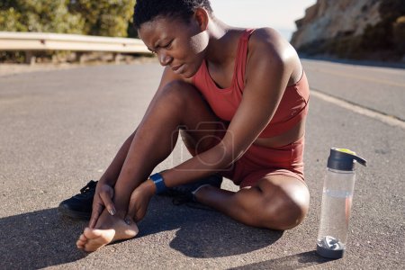 Foto de Mujer negra, corredor y pie lesionado al aire libre, dolor y entrenamiento en carretera, maratón y botella de agua. Mujer afroamericana, chica y atleta con malestar en el talón, sufrimiento y agonía por la aptitud - Imagen libre de derechos