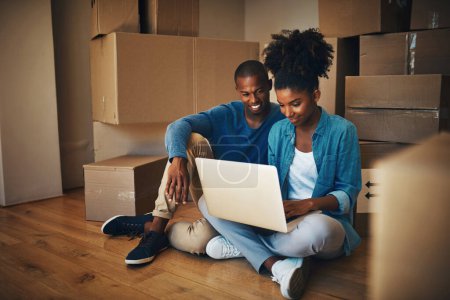 Photo for Paying the bills is so easy these days. a cheerful young couple browsing on a laptop together while being surrounded by cardboard boxes inside at home - Royalty Free Image
