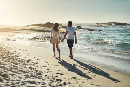 Foto de Disfrutan de largos paseos por la playa. Vista trasera de una pareja joven despreocupada caminando de la mano a lo largo de la playa - Imagen libre de derechos