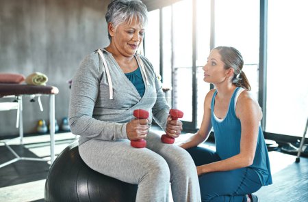 Werden Sie aktiv und werden Sie wieder lebendig. eine Seniorin mit Gewichten und einem Fitnessball mit Hilfe eines Physiotherapeuten