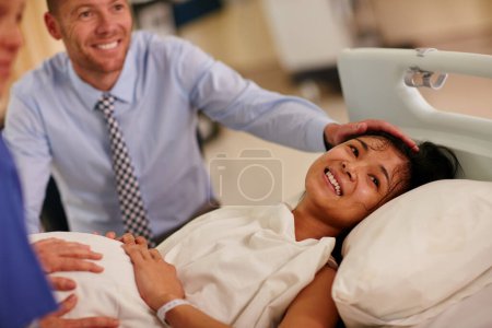 Téléchargez les photos : Tout cela en valait la peine... une jeune femme allongée à l'hôpital avec son mari en arrière-plan - en image libre de droit
