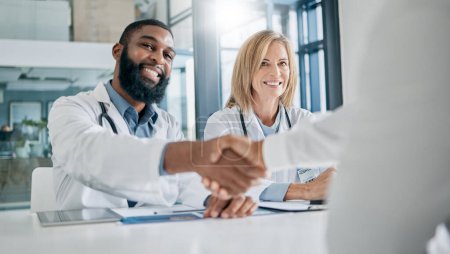 Handshake, partnership or happy doctors in a meeting after successful medical surgery or reaching healthcare goals. Teamwork, woman or black man smiles shaking hands with a worker in hospital office.