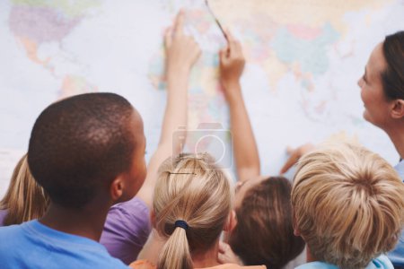 Photo for The world is full of oppurtunities. A group of excited schoolchildren pointing at a world map as their teacher looks on - Royalty Free Image