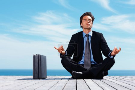 Photo for Business man sitting in lotus position with briefcase on a pier. Smart young business man sitting in lotus position with briefcase on a pier - Royalty Free Image