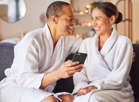 Senior couple, phone and relax spa wellness on sofa, beauty center and luxury body care or streaming video online. Happiness, woman and man smile together for love with smartphone and therapy gown.