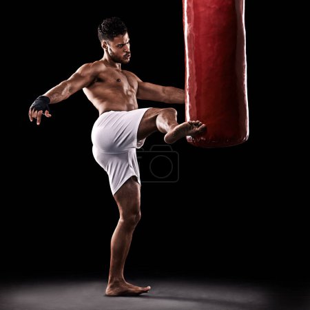 Photo for Give it all youve got. Studio shot of kick boxer working out with a punching bag against a black background - Royalty Free Image