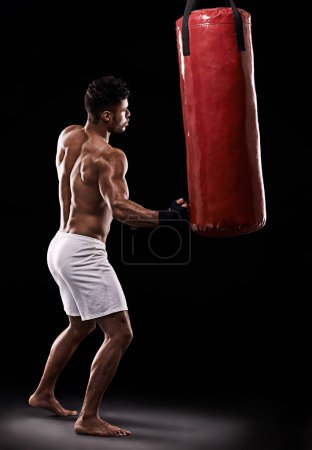 Photo for Strike while the iron is hot. Studio shot of kick boxer working out with a punching bag against a black background - Royalty Free Image