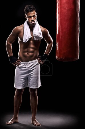Photo for Eat train sleep repeat. Studio shot of kick boxer working out with a punching bag against a black background - Royalty Free Image