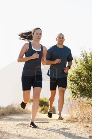 Téléchargez les photos : Running is always better with a partner. a young couple running along a trail - en image libre de droit