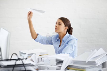 Téléchargez les photos : The day is just not flying fast enough. A young businesswoman throwing a paper plane while sitting at her desk - en image libre de droit