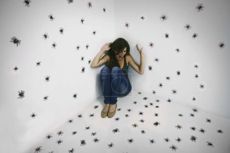 Foto de Arachnophobics worst nightmare come true. A young woman crouched in terror while surrounded by spiders - Imagen libre de derechos