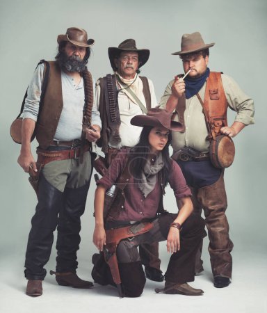 Photo for No one ever bothered to ask how she came to be in the gang...A band of outlaws standing isolated on gray while looking tough - Royalty Free Image