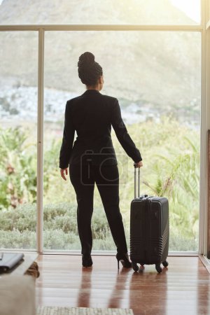 Photo for Travel, luggage and glass with a business black woman standing in a hotel looking at the view. Corporate, window and accommodation with a female employee in a luxury or modern apartment for work. - Royalty Free Image