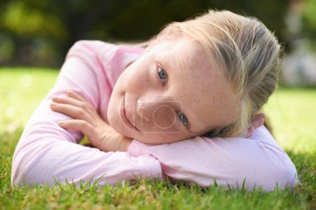 Téléchargez les photos : Enjoying the summer sun. Portrait of a young girl lying on the grass outside - en image libre de droit
