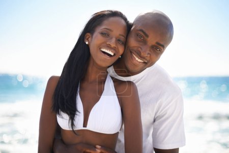 Foto de They couldnt be happier. A happy african-american couple embracing on the beach - Imagen libre de derechos