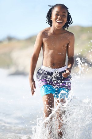 Téléchargez les photos : Awesome. An excited young boy charging through the shallows of the sea - en image libre de droit