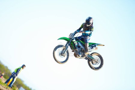 Photo for Smooth landing. A motocross racer in mid-air with a spectator looking on in the background - Royalty Free Image