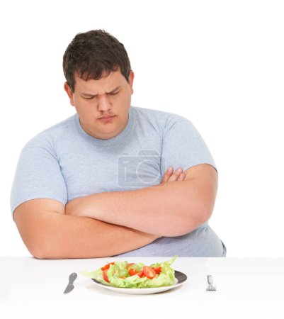 Photo for Aint nobody got time for salad. An obese young man sitting with arms folded at a table with a plate of salad in front of him - Royalty Free Image