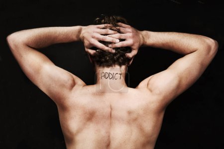 Photo for Branded as an addict. Rear view of a naked young man holding his head with the word addict on the back of his neck - Royalty Free Image