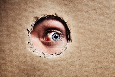 Photo for Through the looking hole. Closeup of an eye looking through a hole in a piece of cardboard - Royalty Free Image