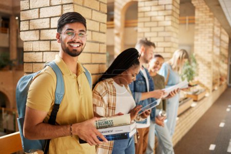 Foto de University, hallway and portrait of Indian man and students standing in row together with books at business school. Friends, education and future, happy man in study group on campus in lobby for exam. - Imagen libre de derechos