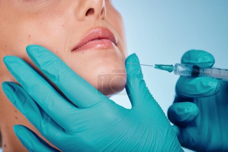 Foto de Botox, hands and cosmetic surgery with a woman and doctor in studio on a blue background for face change. Beauty, skin and injection with a surgeon holding a syringe for female client facial filler. - Imagen libre de derechos
