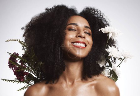 Black woman, beauty and flowers on studio background for healthy skincare. Happy face, floral plants and model with spring perfume, natural makeup and eco wellness for cosmetics, aesthetics and smile.