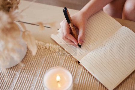 Foto de Hand, candle and woman writing in journal with top view for calm, peace mindset and relax morning routine in home. Hands, notebook and diary planning goals, idea vision or creative writer lifestyle. - Imagen libre de derechos