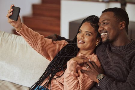 Téléchargez les photos : Black couple, phone selfie and love while together on home couch with care and happiness in a happy marriage. Young man and woman with a smile for social media while bonding in an apartment lounge. - en image libre de droit