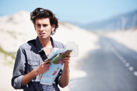 Foto de Where to go from here. Trendy young man standing on the side of the road holding a map and looking puzzled - Imagen libre de derechos