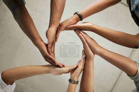 Foto de Close up of a group of colleagues putting hands together to form a circle in the office from below. Creative team joining hands and showing unity in teamwork. - Imagen libre de derechos