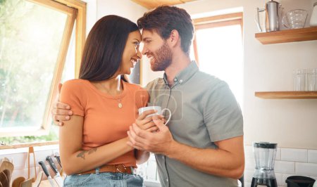 Happy interracial couple bonding while drinking tea together at home. Loving caucasian boyfriend and mixed race girlfriend standing in the kitchen. Content husband and wife relaxing and spending time.