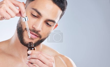 Lets give this bad boy a try. Studio shot of a handsome young man applying serum to his face against a grey background