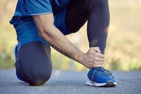Téléchargez les photos : Ankle pain is a result of poor running shoes. an unrecognisable man kneeling and suffering from a sprained ankle during his outdoor workout - en image libre de droit