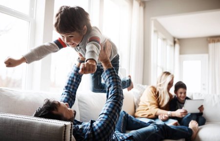 Foto de Family, father and lifting child on sofa for bonding, wellness and play in happy home. Dad playing flying plane in air game with son on living room couch for care, love and bond together. - Imagen libre de derechos