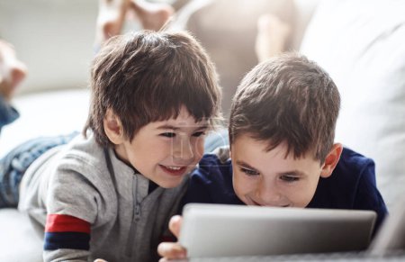 Téléchargez les photos : Happy children, bonding or tablet on relax house sofa in home living room on brothers esports, social media or movies. Smile, fun or kids streaming on digital technology in team education or learning. - en image libre de droit