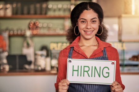 Téléchargez les photos : Portrait, small business or black woman with hiring sign for onboarding in a cafe or coffee shop with hospitality. Restaurant manager with a happy smile with recruitment message after opening store. - en image libre de droit