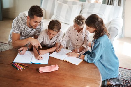 Foto de Nothing encourages learning like a supportive family. a happy young family of four doing homework together - Imagen libre de derechos
