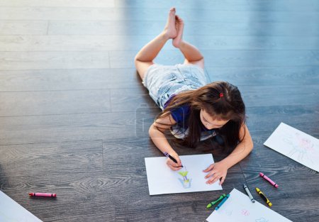 Foto de Shes living a life full of color. Full length shot of a young girl lying down on the floor and coloring in pictures in her coloring book at home - Imagen libre de derechos