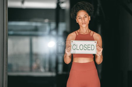 Téléchargez les photos : Fitness, portrait or personal trainer at gym with a closed sign for workout exercises or training. Manager, bankruptcy or serious black woman holding a board to stop exercising in empty health club. - en image libre de droit
